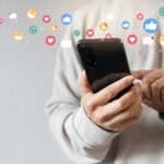 Une personne utilise un smartphone entouré d'emojis, illustrant l'interaction sociale numérique et l'utilisation des réseaux sociaux.