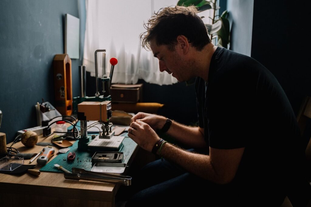 A craftsman carefully works on leather goods in a dimly lit home workshop.