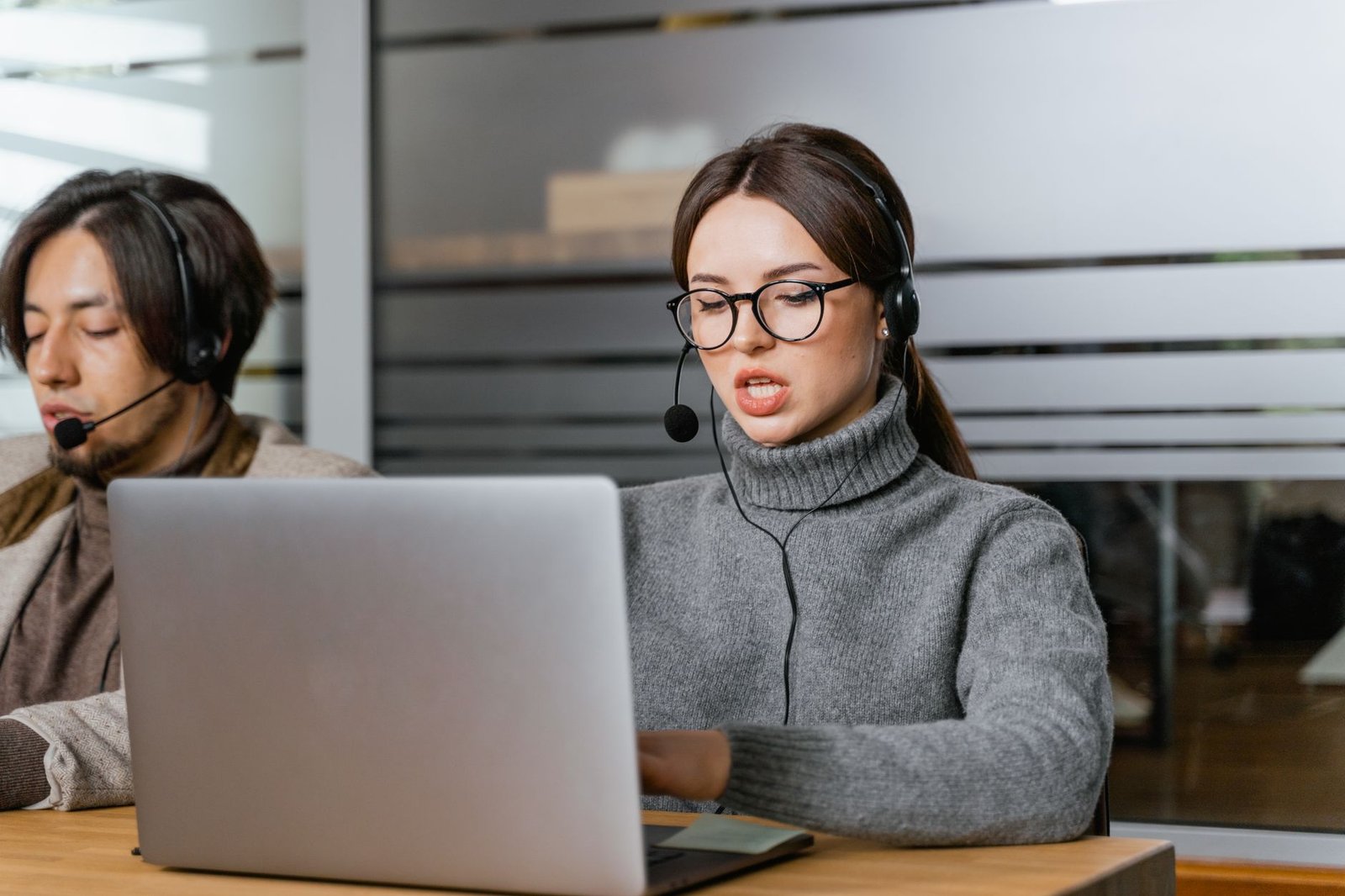 Customer support agents wearing headsets working on laptops in a modern office setting.